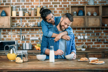 Smiling young woman hugging handsome bearded man having breakfast at home - obrazy, fototapety, plakaty