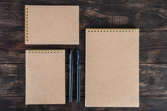 Set of three spiral notepads with two black pens on wooden table. Top view with copy space