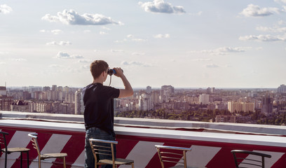 Young man looking through binoculars on the roof of a building