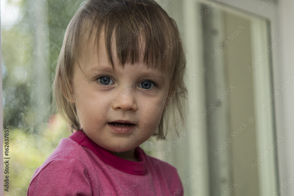 Wall mural Cute little toddler girl portrait by the window