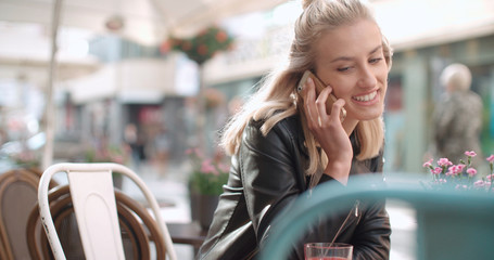 Portrait of young caucasian woman using phone while sitting at cafe, outdoors.