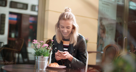 Portrait of young caucasian woman using phone while sitting at cafe, outdoors.
