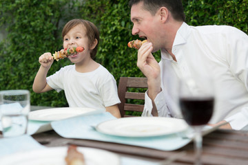 Father with little bcute boy eating barbecue in family lunch time at home.