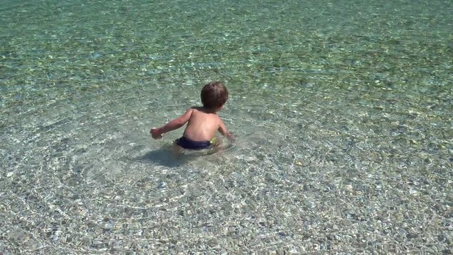4K Little boy collects stones in the sea 