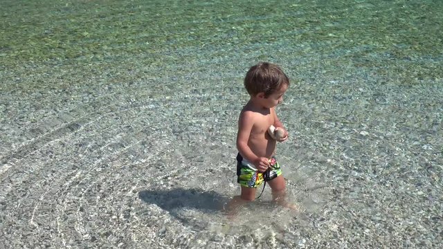 4K Little boy collects stones in the sea 