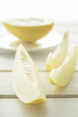 Melon cut into pieces on a white wooden table. A high key.