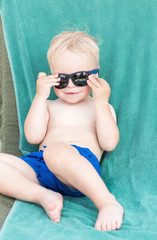 Blond toddler boy wearing sunglasses on a beach