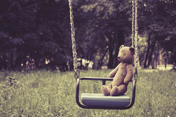Old toy teddy bear sitting on swing in park