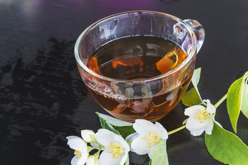 glass cup of tea and jasmin flowers on dark backgorund