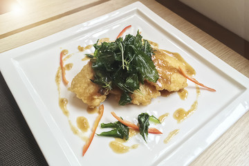 Spicy Fried Fish with green vegetable and slice of red sweet pepper on white plate.