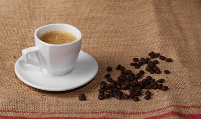 pile coffee beans and white cup on jute background, texture
