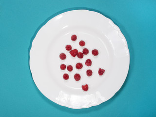 Berries of ripe raspberries on a white plate on a blue background 
