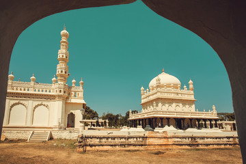 View from arch on the tall stone minaret and historical Tipu Sultan Gumbaz in Srirangapatna, India. 18th century Muslim mausoleum.