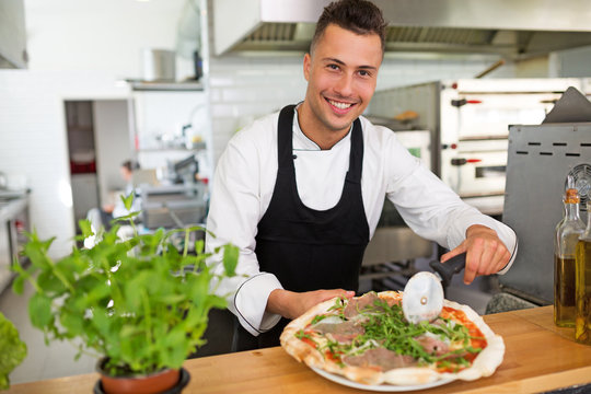 Smiling chef preparing pizza in kitchen
