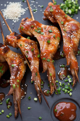 Close-up of skewers with barbecued chicken wings with sauce, sesame and green onion, selective focus