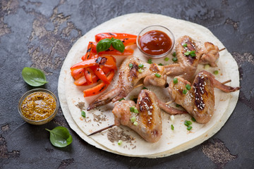 Tortillas with grilled chicken wings on skewers, vegetables and sauces, horizontal shot on a brown stone background