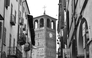 A ancient belfry between old buildings in Pinerolo, Italy. Black and white.