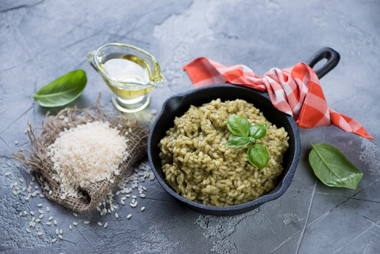 Frying pan with spinach risotto and raw rice, horizontal shot over grey stone surface