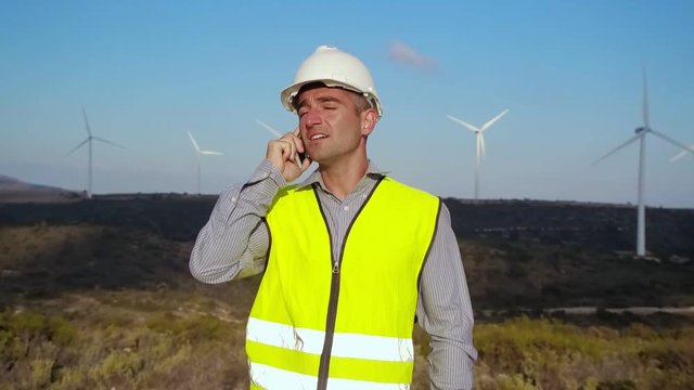 Employee of wind power on the phone on the background of windmills
