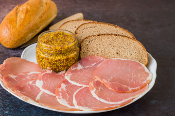  Fast snack. Smoked bacon, sliced thin slices, bread and mustard on a white porcelain dish on a...