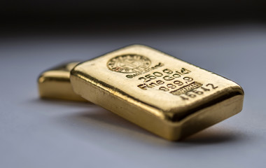 Two cast gold bars on a grey background. Selective focus.