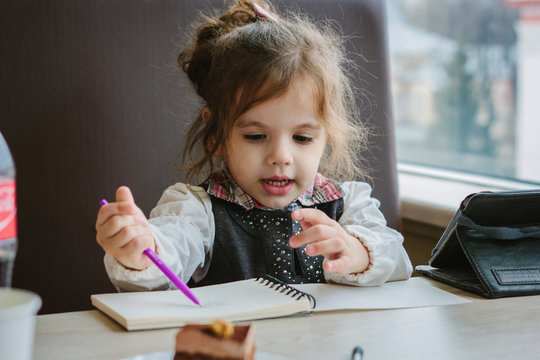 Little kid girl writing or drawing with pen in scetch book