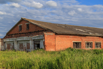 Abandoned building of red brick, overgrown with grass