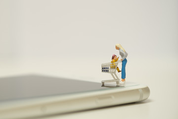 Miniature shopper standing on smart phone with cart ,easy to buy goods or services from a seller over the internet. Online shopping concept  with copy space