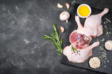 Raw poultry meat. Duck legs with rosemary, spices and olive oil on cutting board over dark...