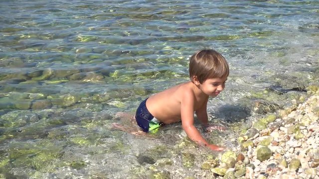 4K Two and a half years old boy Boy kneels down and crowls in the sea