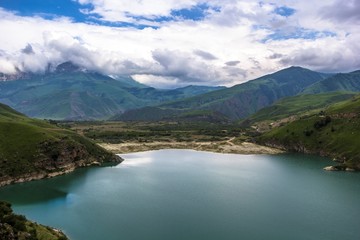 Fototapeta na wymiar Горный пейзаж, красивый вид на живописное озеро в горном ущелье, облачная погода, зеленые склоны, дикая природа и горы Северного Кавказа