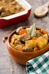 Beef meat stewed with potatoes, carrots and spices in ceramic bowl on wooden table
