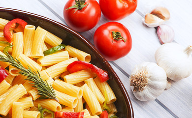 Close-up view of bowl with vegetable pasta served on table with fresh tomatoes and garlic.