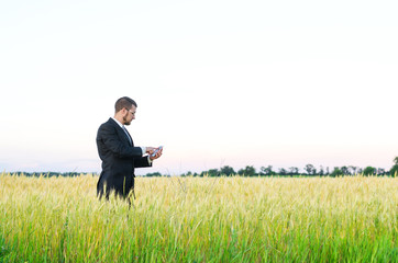 Naklejka na ściany i meble Businessman with a smartphone in a wheat field, a copy of the free space.