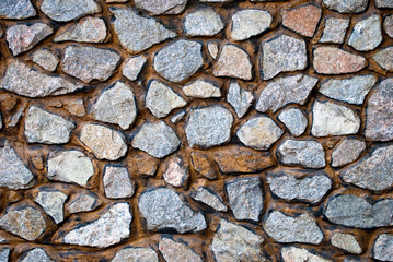 Large wall of natural granite stones of different size and color gray texture on a summer day