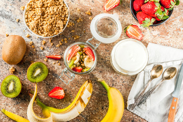 Healthy breakfast. Diet. Overnight oatmeal in a can, muesli. Yogurt with homemade granola and organic fruits - kiwi, banana, strawberry. On the stone table. With ingredients and spoons.
