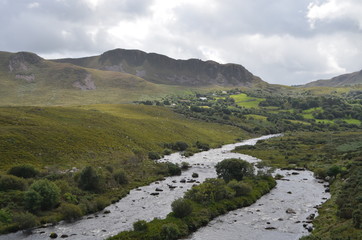 Fototapeta na wymiar Small River Flow in Green Vegetation and Mountain Landscape in a National Road in Ireland