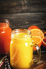 Refreshing summer drink. Juice from classic oranges and red Sicilian oranges. On a rustic wooden table, with whole and cut oranges. Copy space
