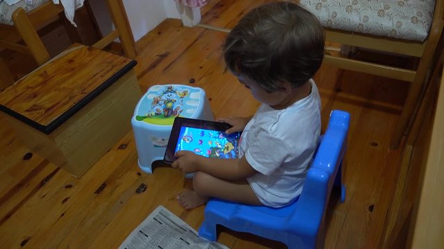4K Child playing with tablet sitting on potty