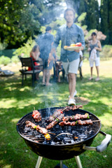 close up of a barbecue grill with meat and sausages cooking during summer garden party with people...