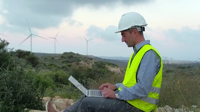 Employee of wind power working at a computer on a background of windmills