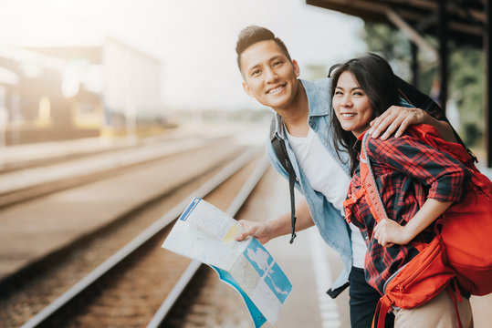 Happy Asian couple traveler holding a map at train station waiting for train
