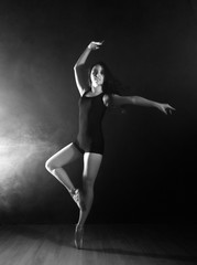Fototapeta premium young beautiful ballet dancer in pointe shoes, dancing in a smoke on a dark background. black and white