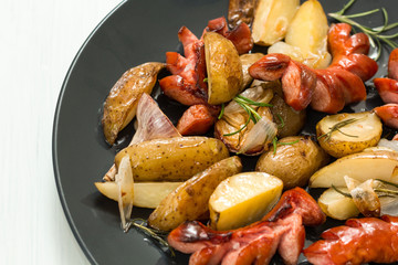 Sausage with fried potatoes and vegetables on a black plate