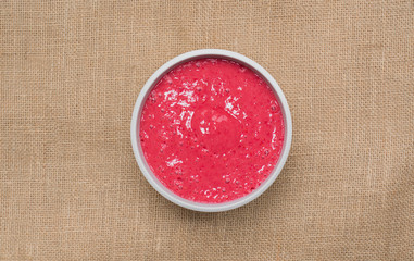 Bowl of fresh fruit sorbet smoothie made with frozen raspberries, bananas and apple juice on a sack cloth hessian background