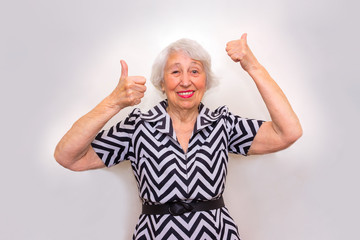 The portrait of a cheerful senior woman gesturing victory over pink