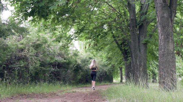 Young woman runs in summer park. Jogging in nature.