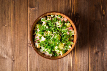 Okroshka. Traditional Russian summer cold soup with sausage, vegetables and kvass in bowl on wooden background.