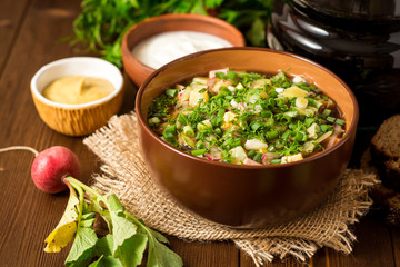 Okroshka. Traditional Russian summer cold soup with sausage, vegetables and kvass in bowl on wooden background.