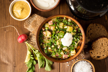Okroshka. Traditional Russian summer cold soup with sausage, vegetables and kvass in bowl on wooden background.
